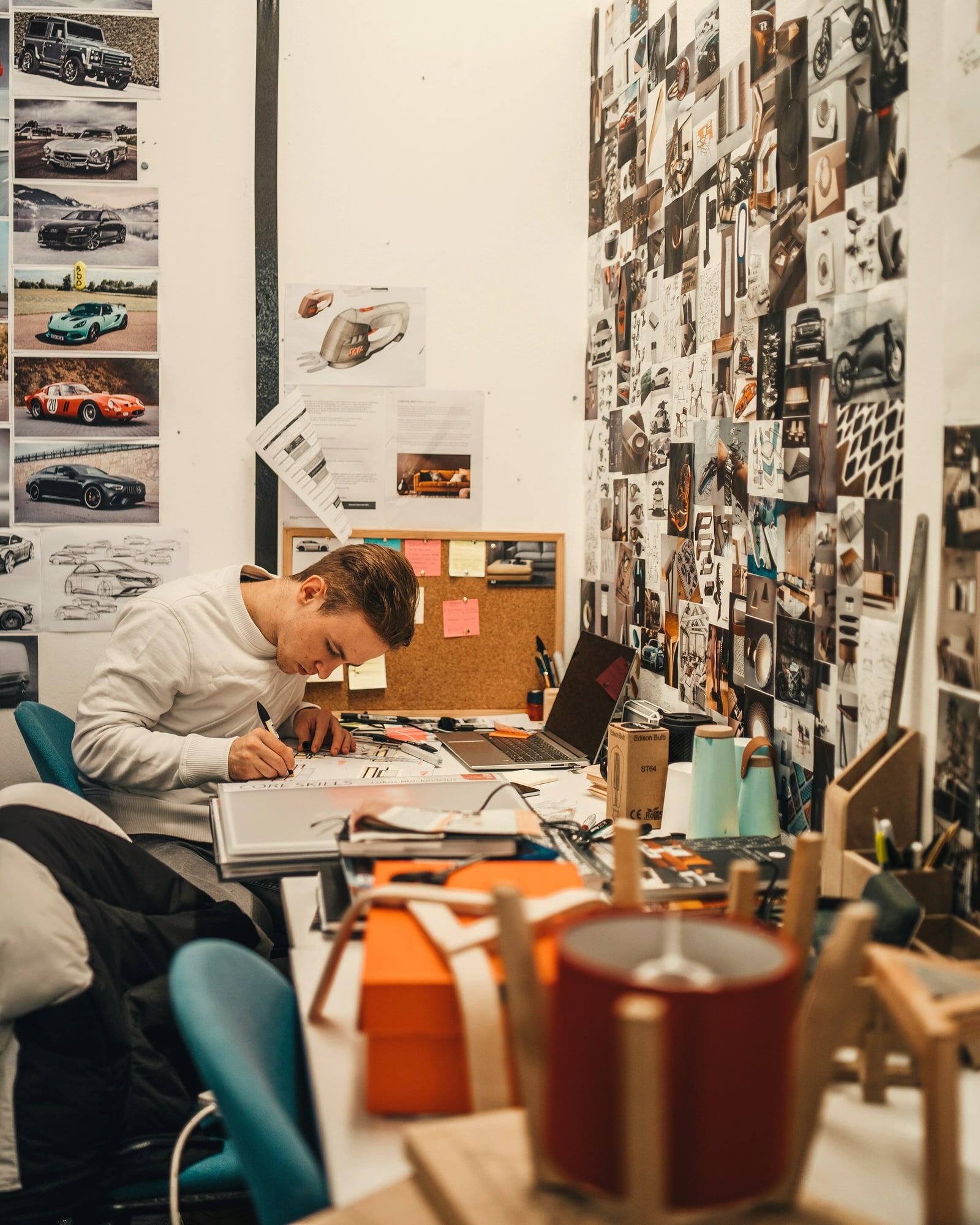A designer sketching at a desk, the wall behind them covered floor to ceiling with printed reference images.
